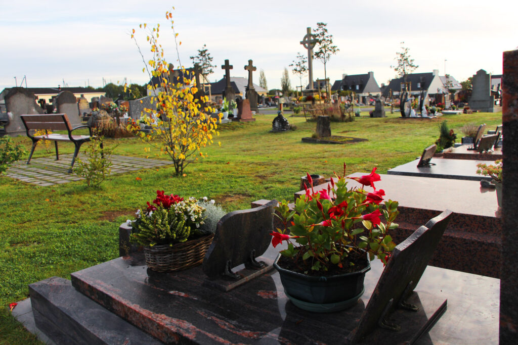 Photo prise dans un cimetière végétalisé, quelques tombes, arbres et bancs