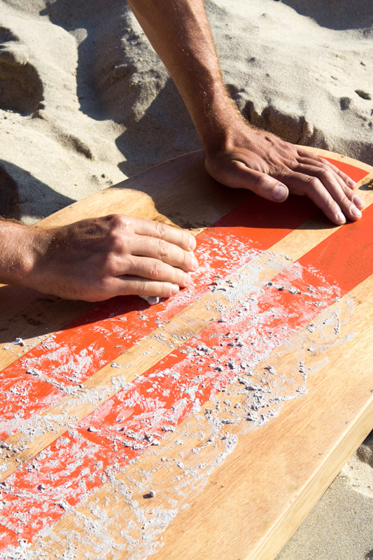 Gros plan sur des mains frottant une planche de surf en bois avec de la wax.