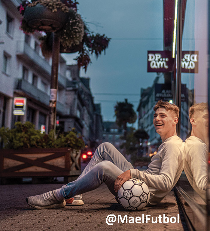 Un jeune homme assis dans la rue avec un ballon de football à la main. Il sourit