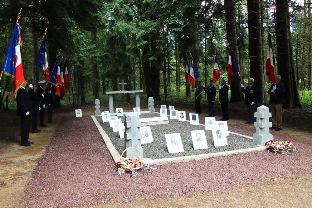 Dans une foret, un lieu de commémoration. Sur les cotés des personnes portant des drapeaux français