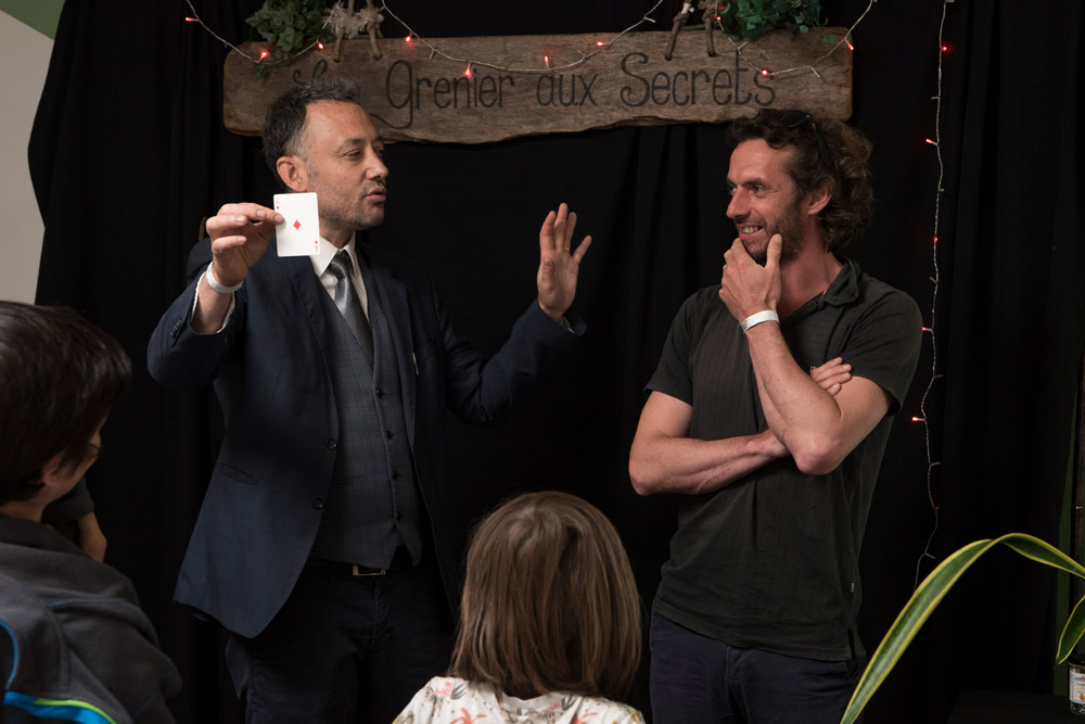 Un magicien montre une carte à jouer devant un petit public lors d’un spectacle au « Grenier aux Secrets ».