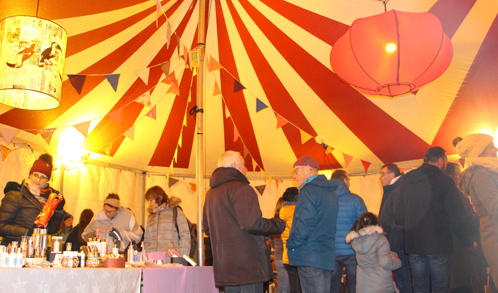 Des visiteurs échangent sous un chapiteau décoré de fanions lors d’un marché ou événement festif.