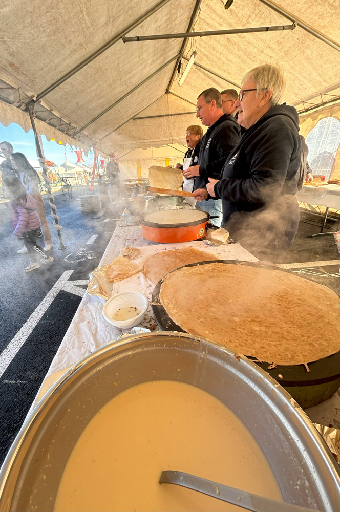 Des bénévoles préparent des crêpes sur des biligs sous une tente lors d’une fête locale.
